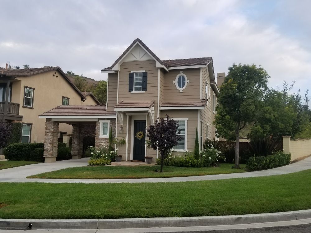 Two-story house with beige siding, dark door, green lawn, and a stone-covered carport.