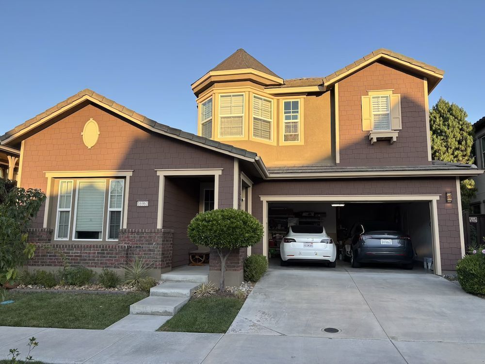 Brown two-story house with a turret and attached garage. Two cars are parked inside.