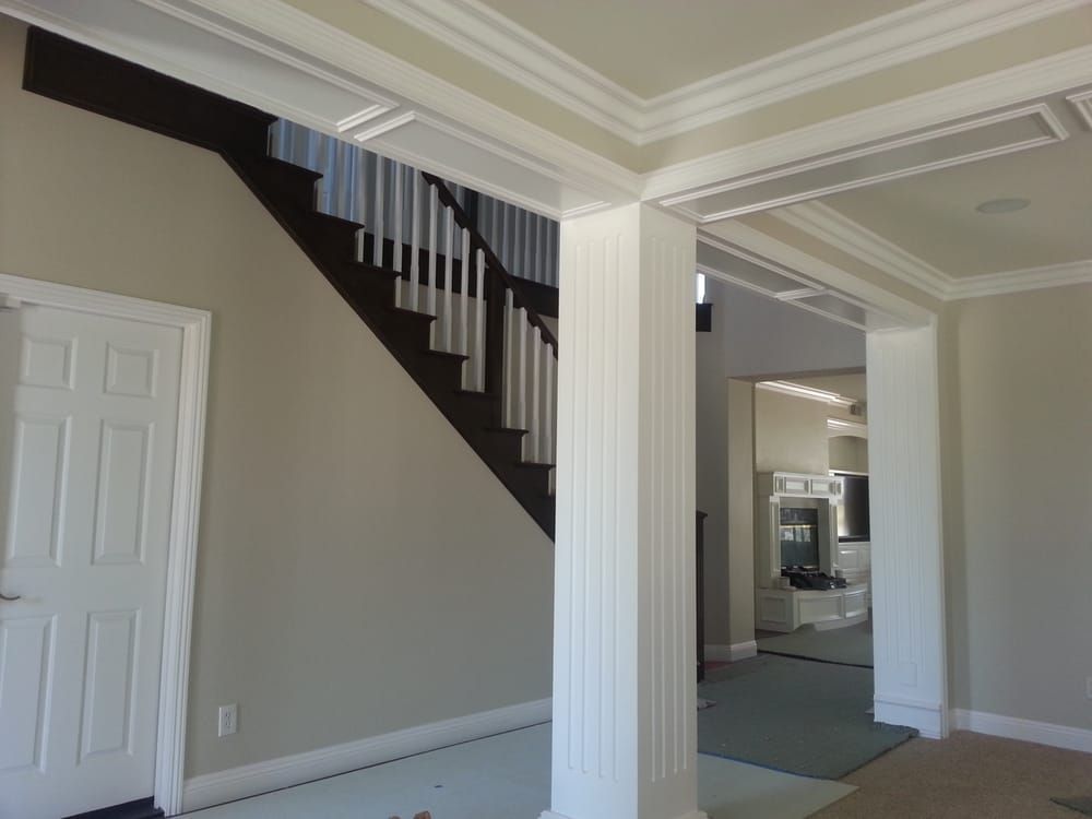 Interior view of a house with stairs, a white pillar, and doorway to another room with a fireplace.