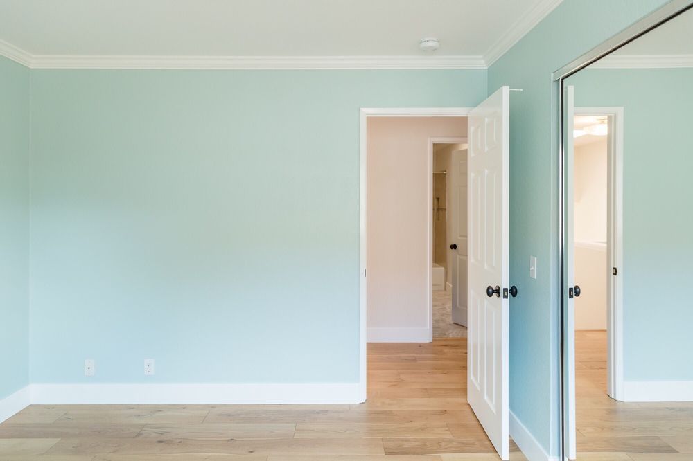 A room with light blue walls, white trim, hardwood floor, and a partially open white door.