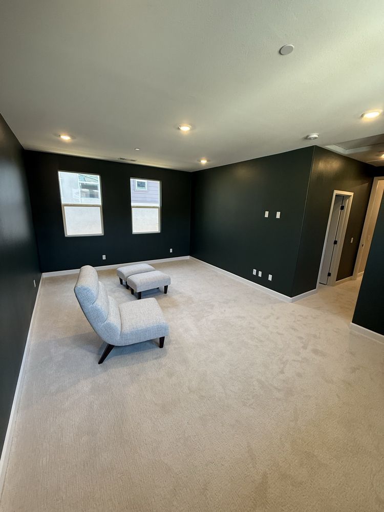 Spacious room with dark green walls, two windows, and light gray carpet; two gray armchairs and ottomans.