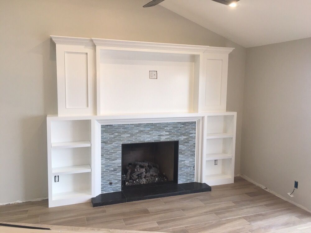 Fireplace with white built-in shelving, blue stone surround, and black hearth, in a room with light wood-look flooring.