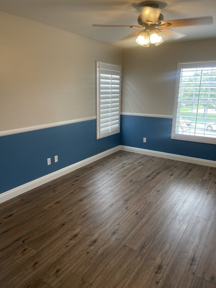 Empty room with blue wainscoting, white trim, wood-look floor, and a ceiling fan.