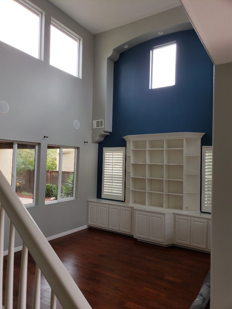 Two-story living room with blue accent wall, built-in white shelves, and wooden floors. Staircase in the foreground.