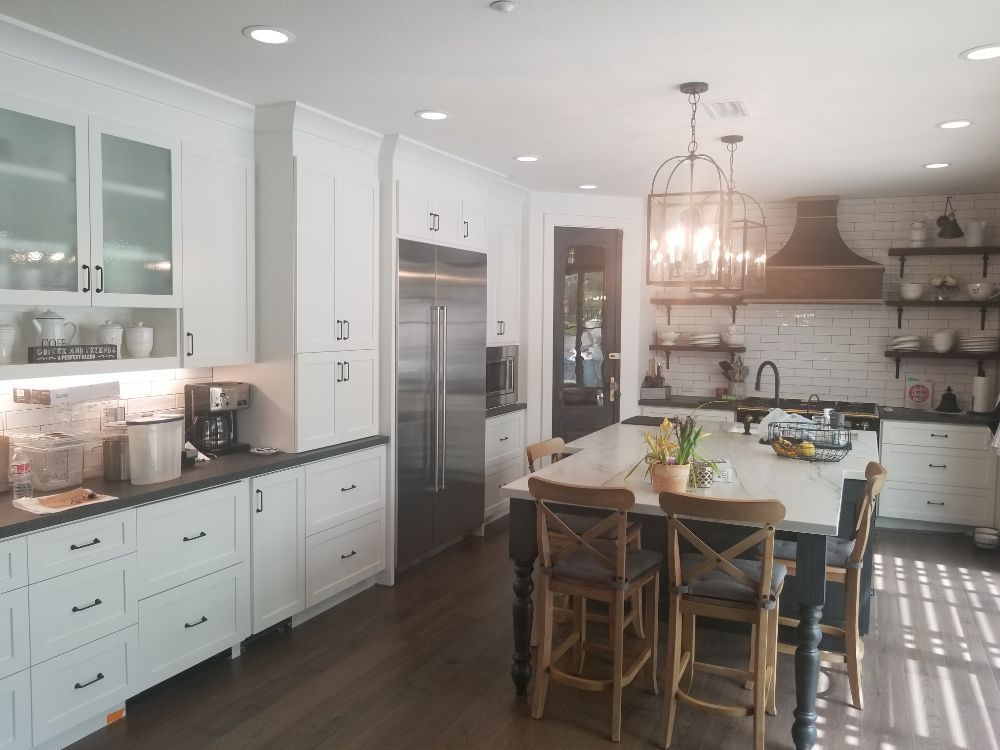 Bright white kitchen with island, black accents, stainless steel appliances, and wooden floors.