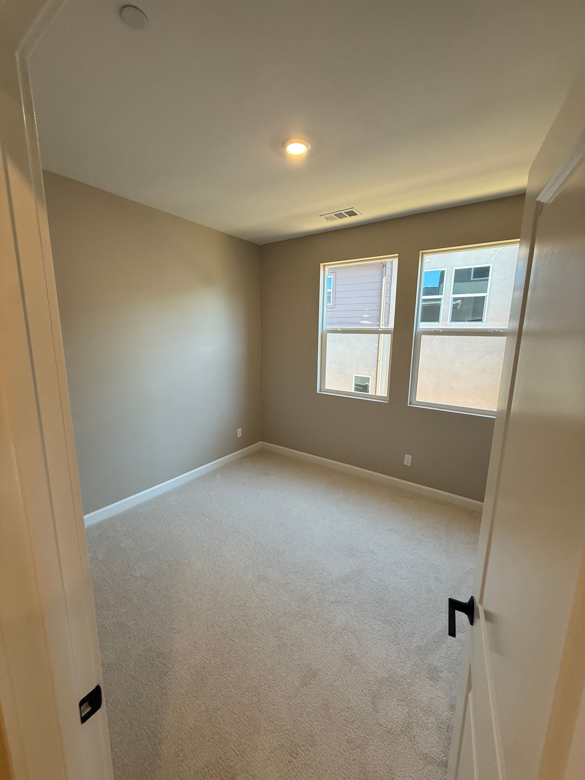 Empty bedroom with beige walls, carpet, two windows, and an open door.