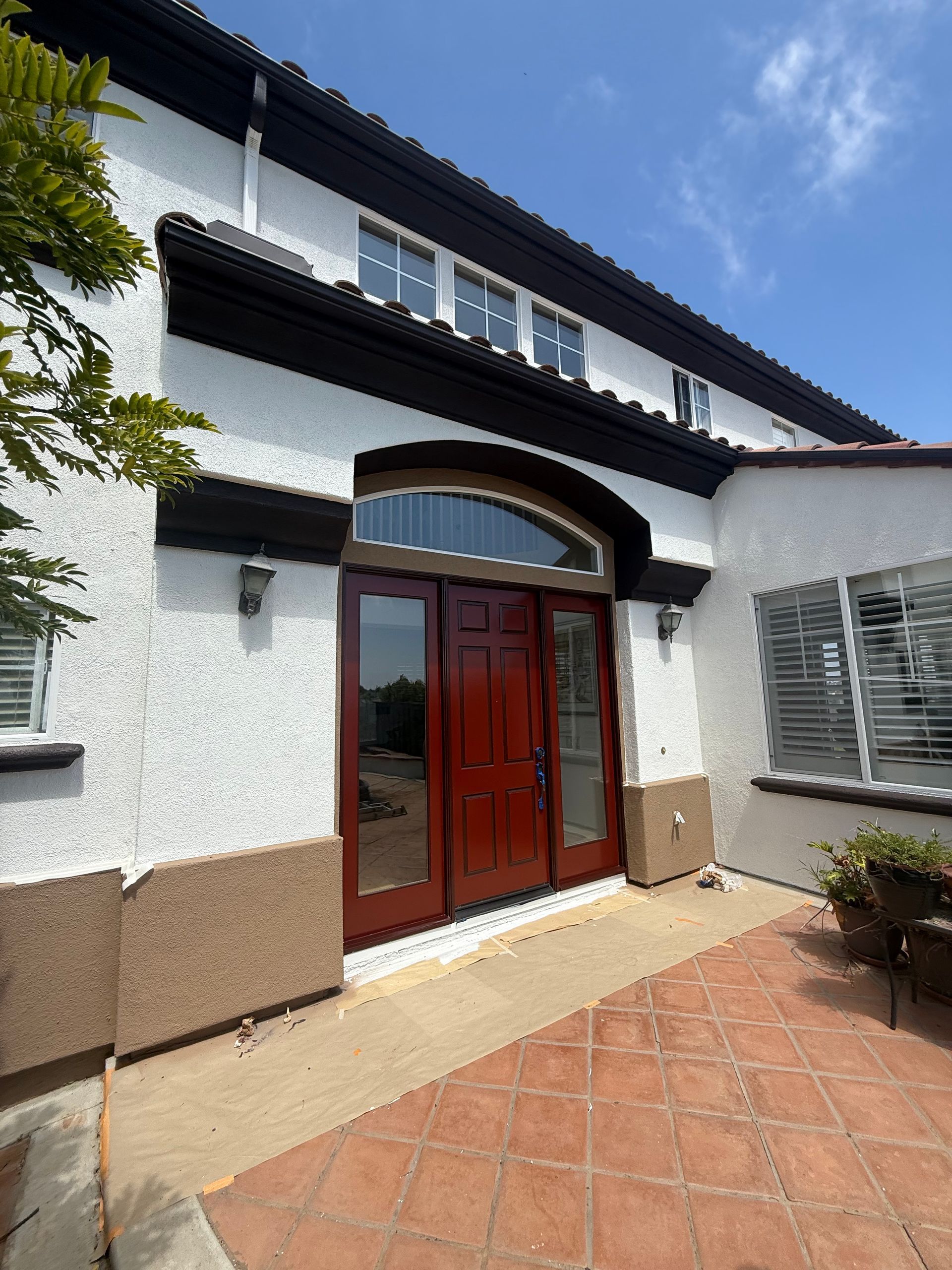 Red double doors under an archway, white stucco exterior with dark trim, terracotta patio.