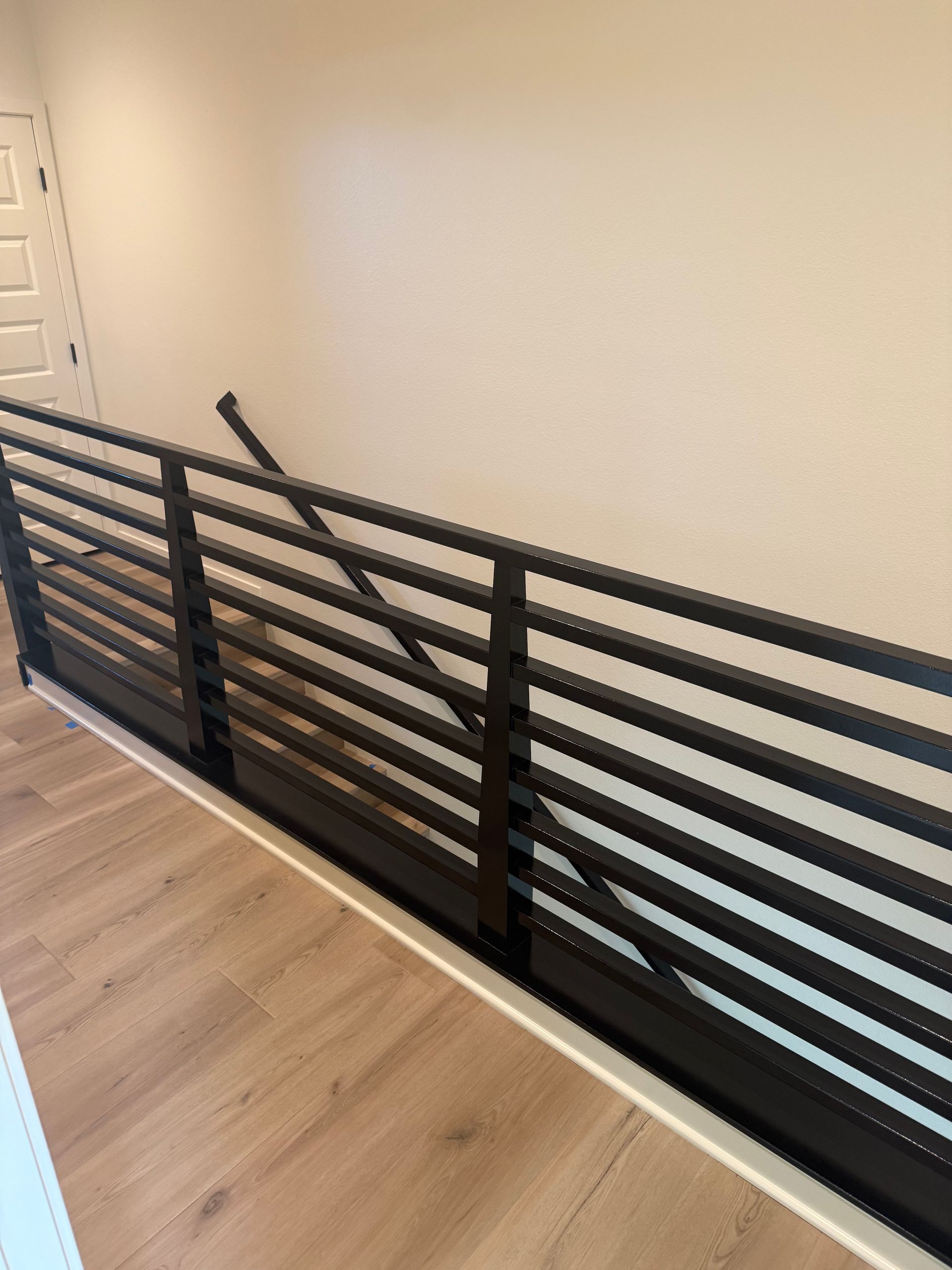 Black metal railing on a landing with horizontal bars. Light-colored flooring and wall.