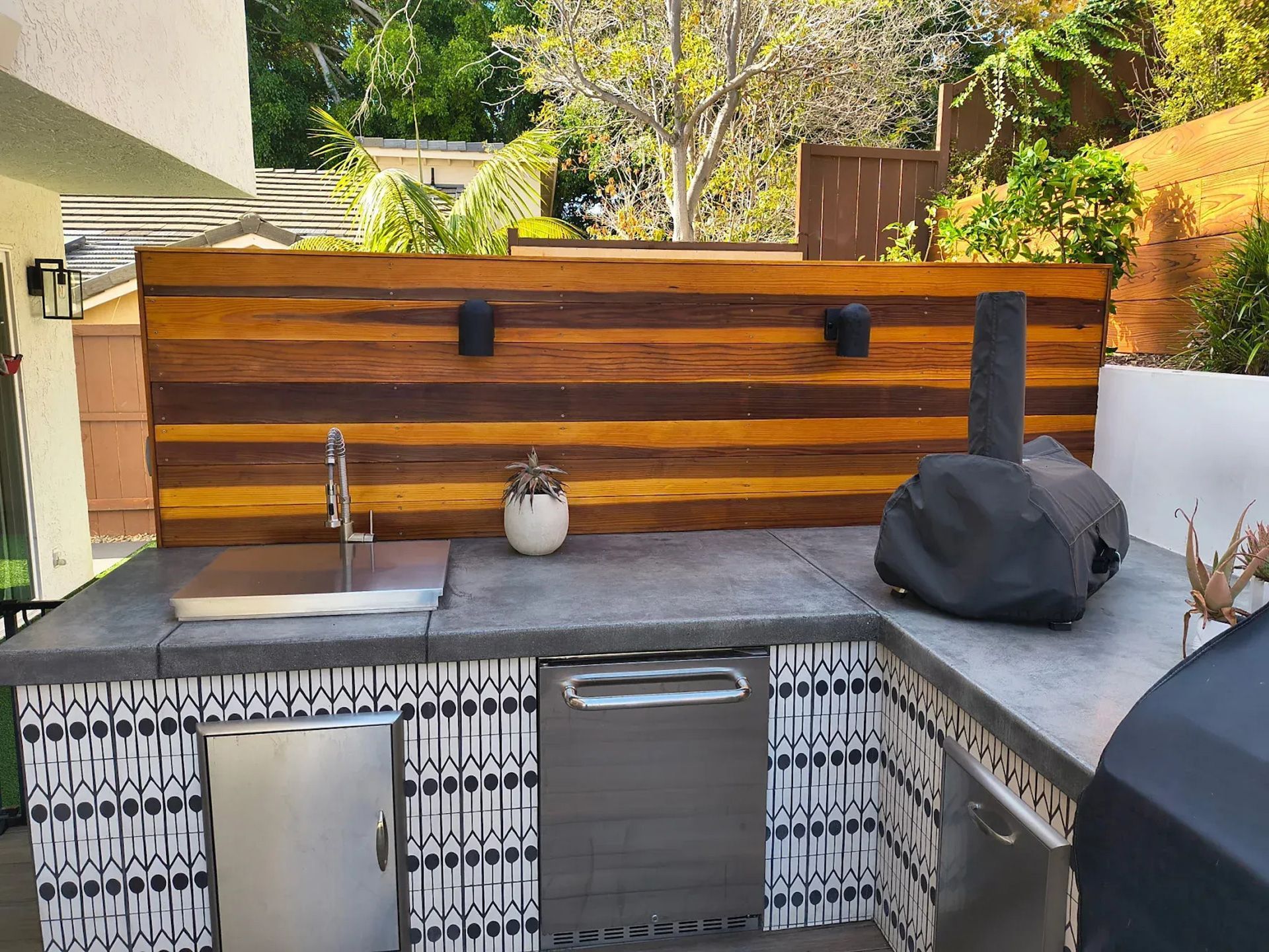 Outdoor kitchen with concrete countertop, wood backsplash, sink, and pizza oven.