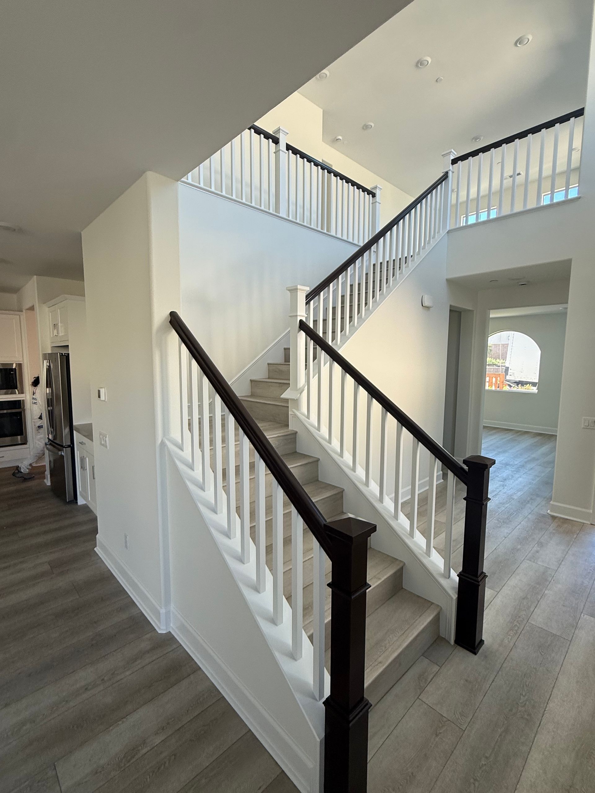 A staircase with dark wood railings and white spindles, leading to a second-floor landing in a brightly lit modern home.