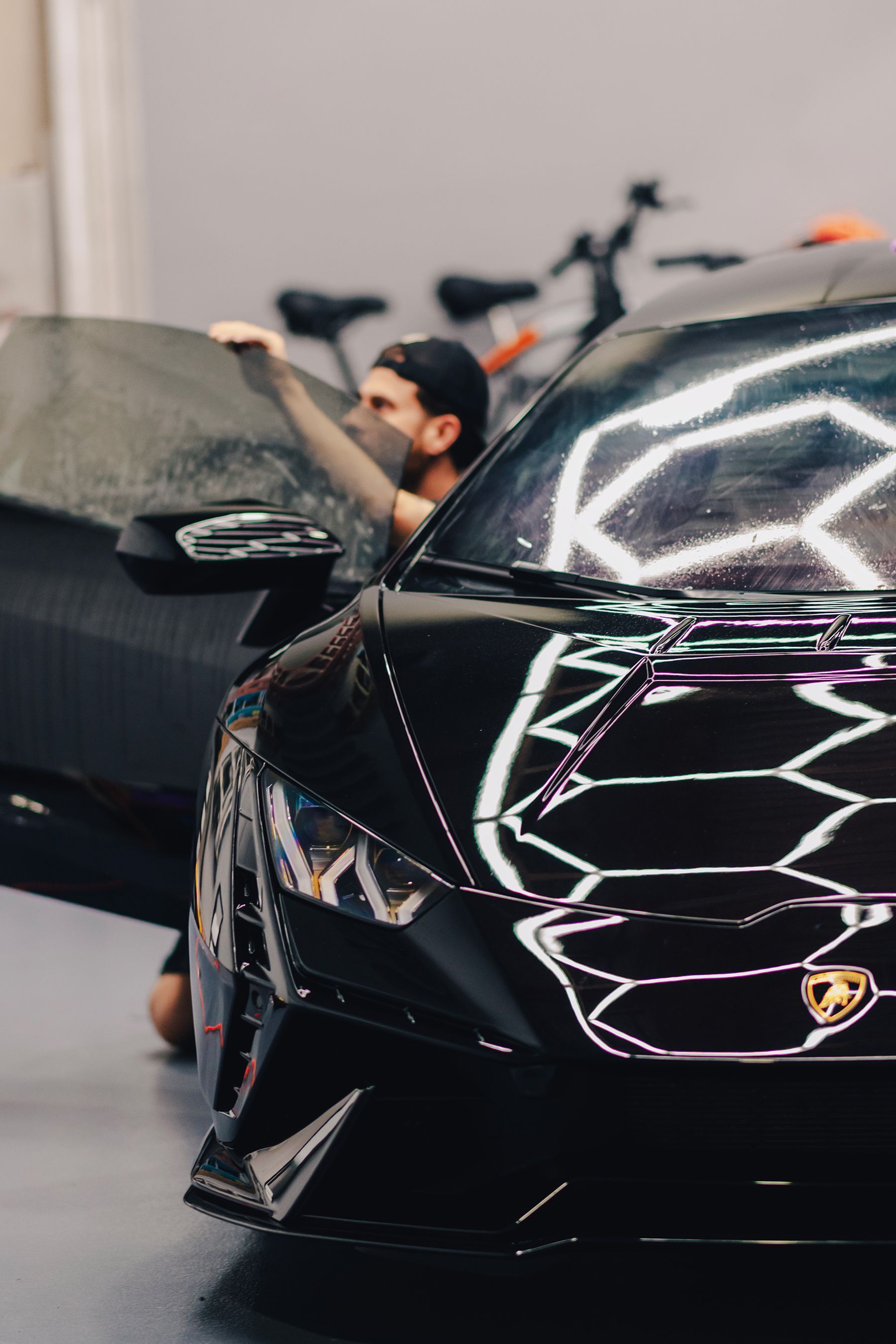 Man applying film to black Lamborghini window. Shop setting.