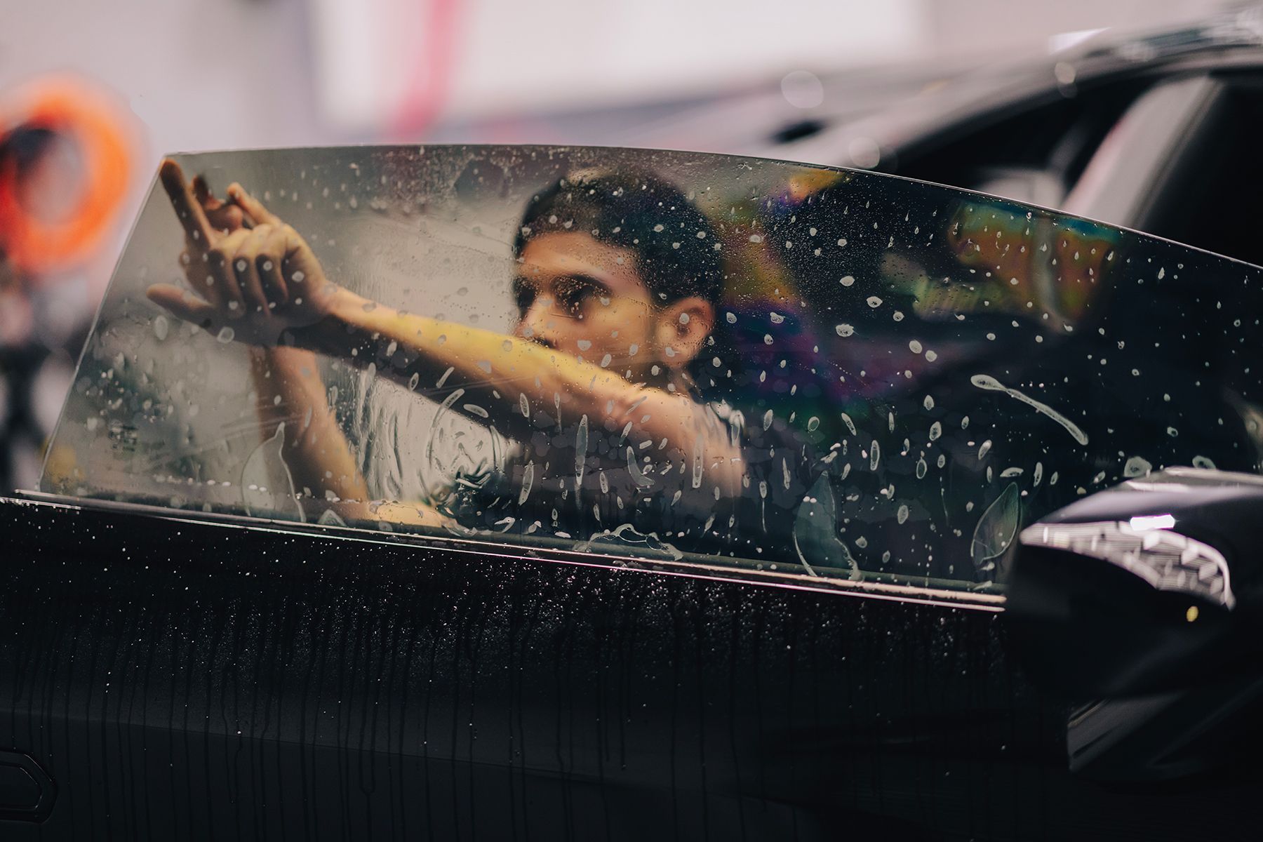 Man applying window tint to a black car, water droplets present.