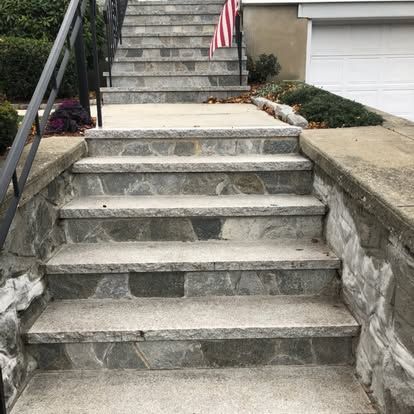 Stone front steps with concrete handrails leading to a home entrance, with a small American flag and garage visible.