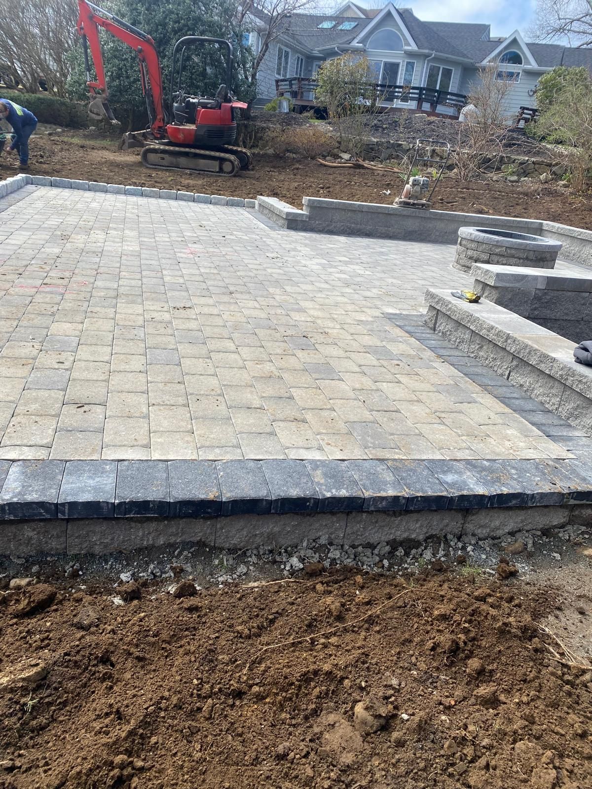 Stone patio under construction with an excavator and houses in the background