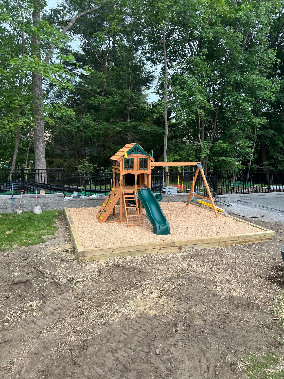 Children’s playground with orange-and-green slide set on a sand base in a wooded park.