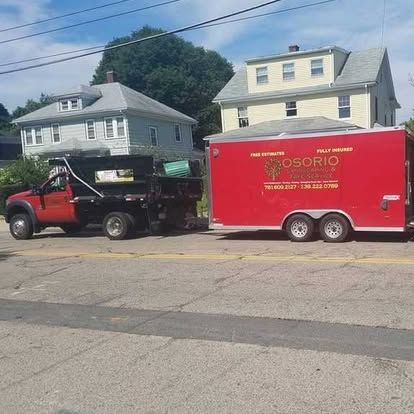 Red truck towing a red trailer parked on a residential street with houses in the background