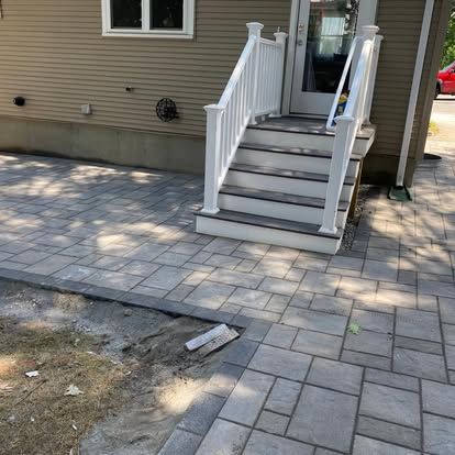 Front steps with white railings leading to a house entrance beside a paved patio and bare dirt area