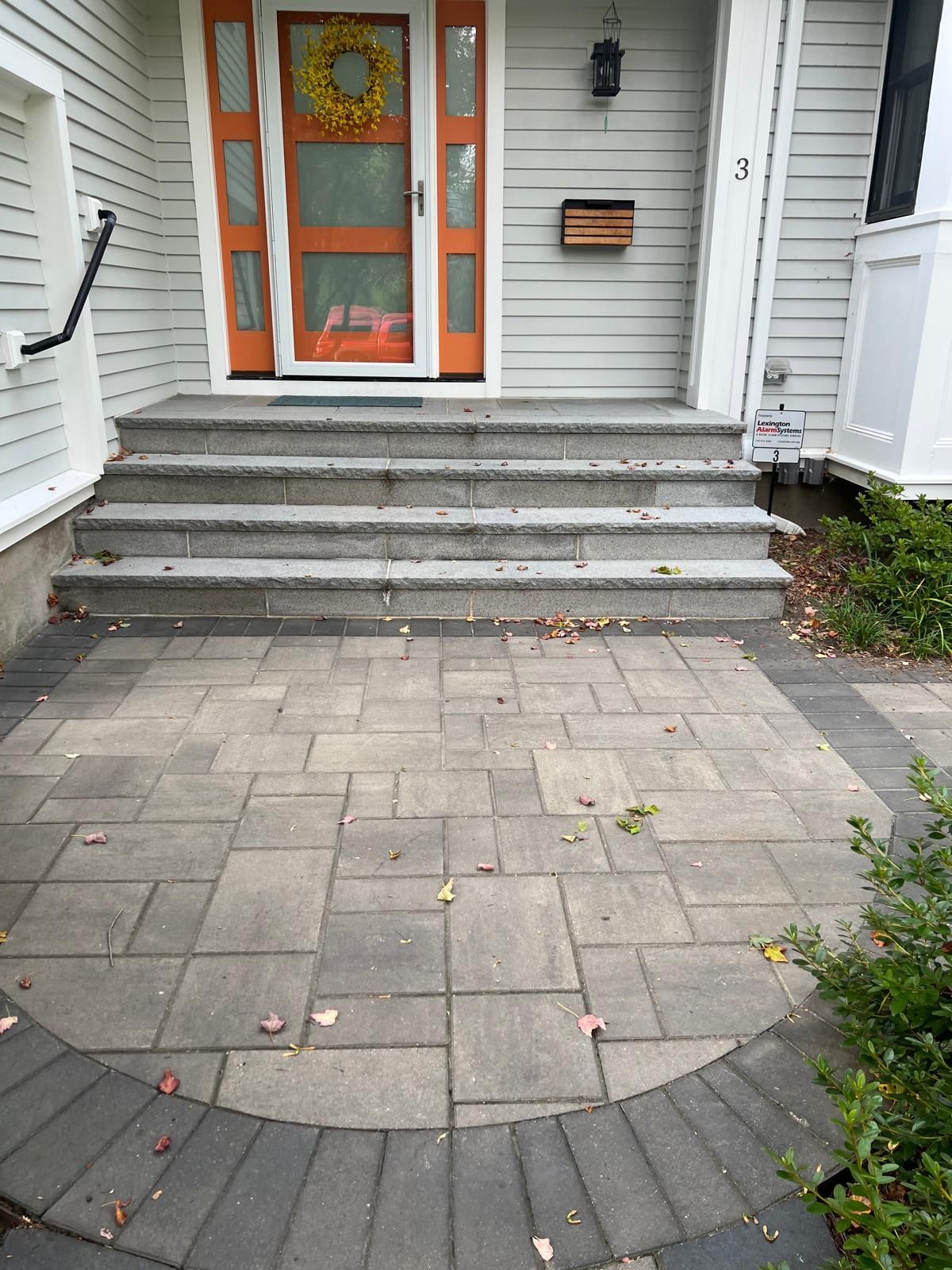 Front steps to a gray house with orange-trimmed double doors and a stone paver walkway.