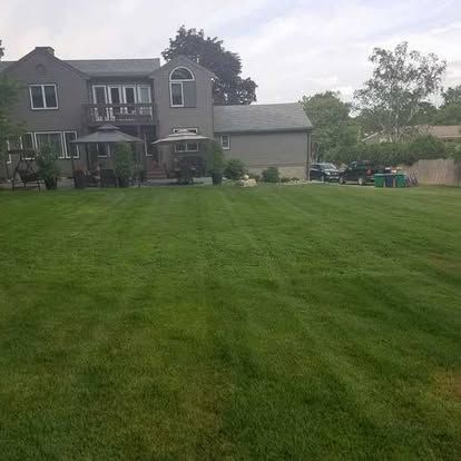 Large gray house with a wide green lawn and trees under an overcast sky