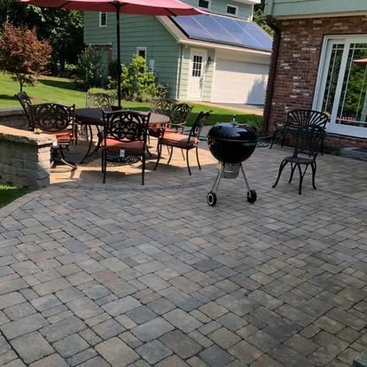 Patio with metal chairs, a black charcoal grill, and paver stone flooring beside a house