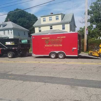 Red Osorio trailer parked on a residential street beside a black truck and houses