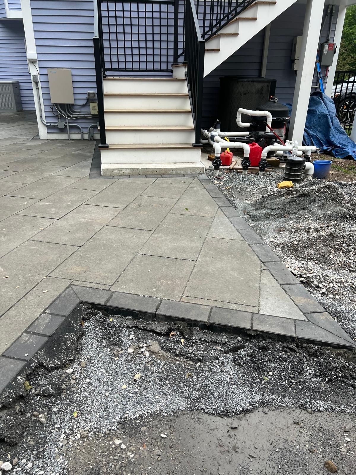 Damaged sidewalk in front of a house stairs, with a broken asphalt patch and construction tools nearby