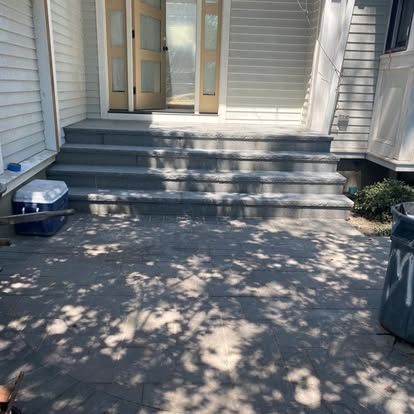 Front porch with gray steps, white siding, glass doors, and dappled tree shadows on the concrete patio.