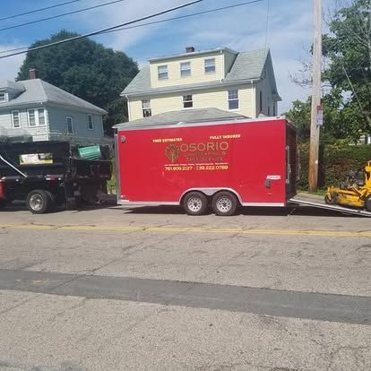 Red Osorio trailer parked on a street beside a black truck, with houses and trees in the background.