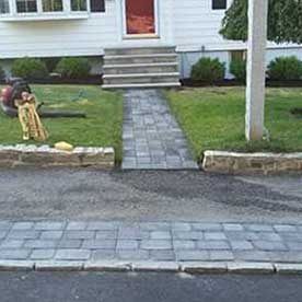 Front yard with a stone walkway leading to a house entrance, and a small lawn mower near the lawn.