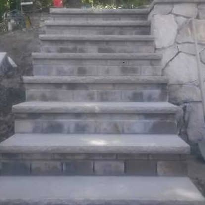 Concrete outdoor stairs leading upward beside a stone wall and greenery