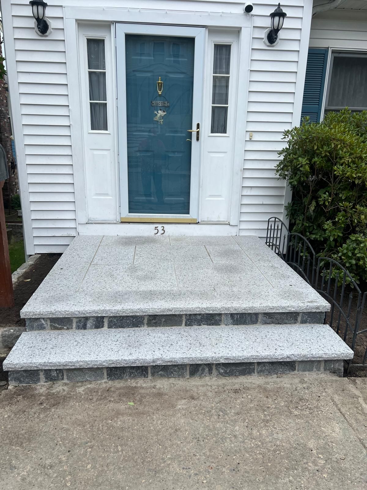 Front porch with two concrete steps and a blue front door on a white house