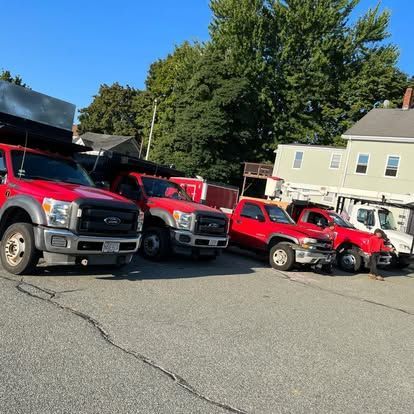 Four red utility trucks parked in a lot beside a beige house on a sunny day