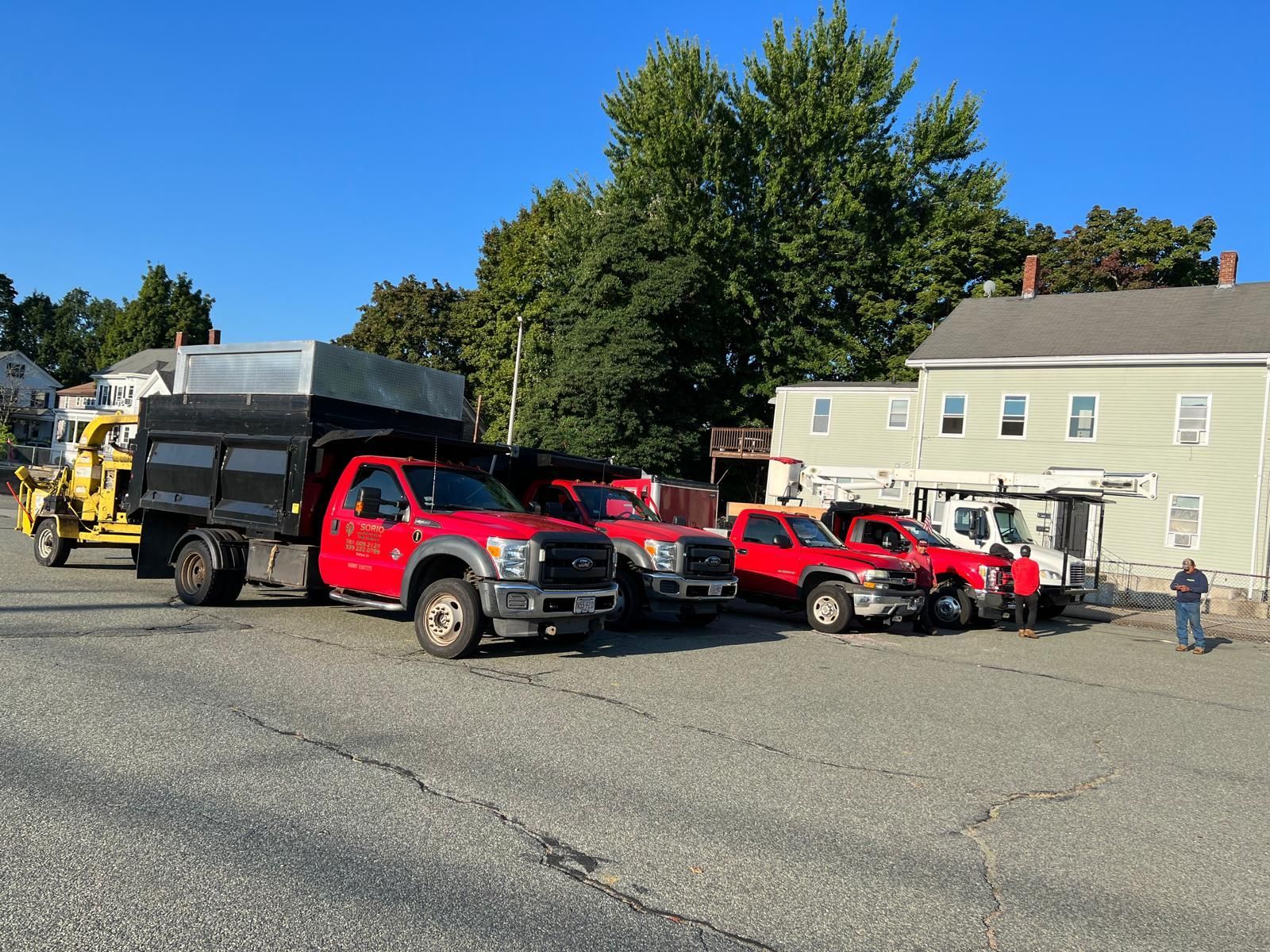 Red tow trucks and a yellow loader parked in a lot beside a beige building