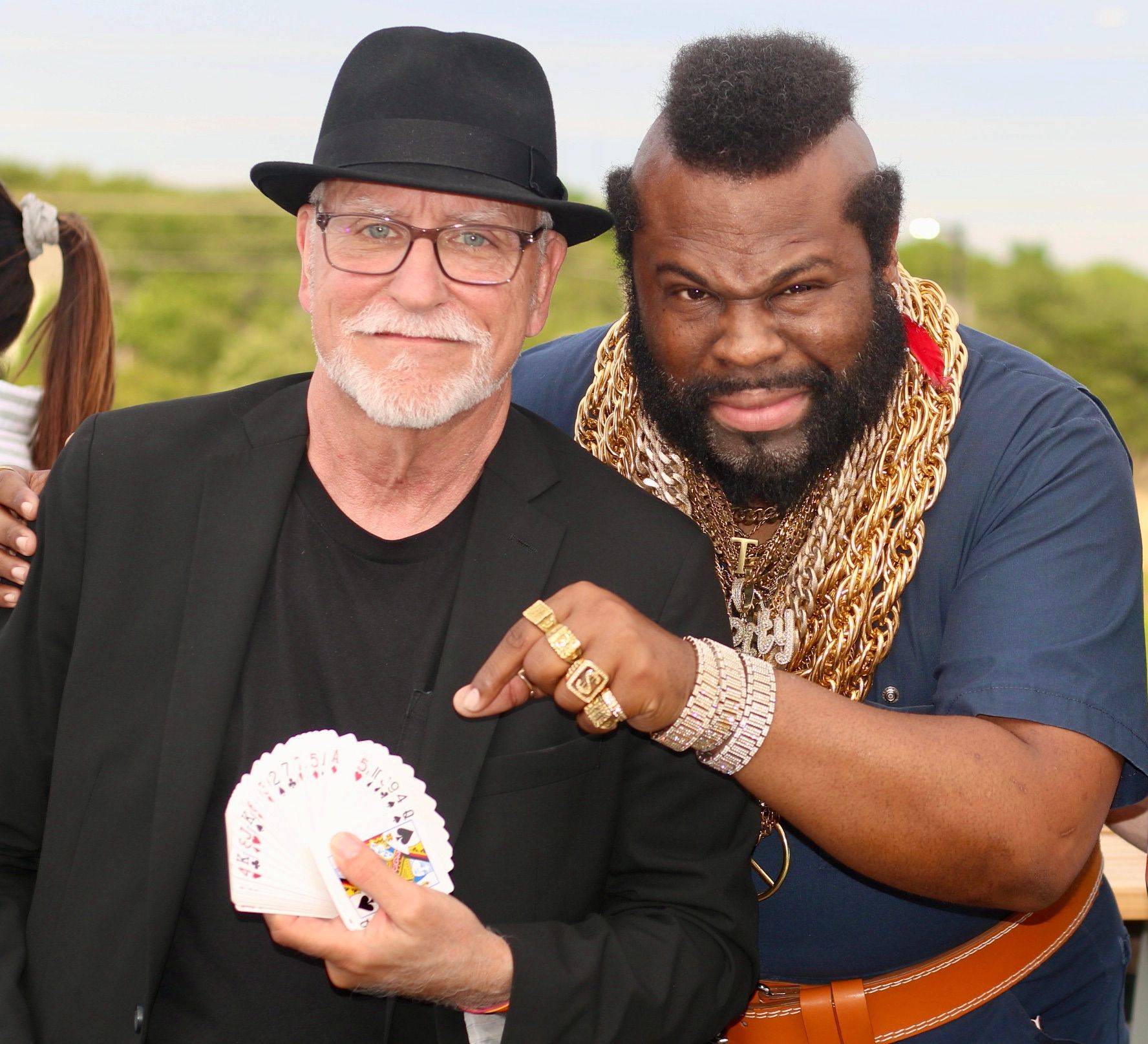 Two men are posing for a picture and one is holding a deck of cards.