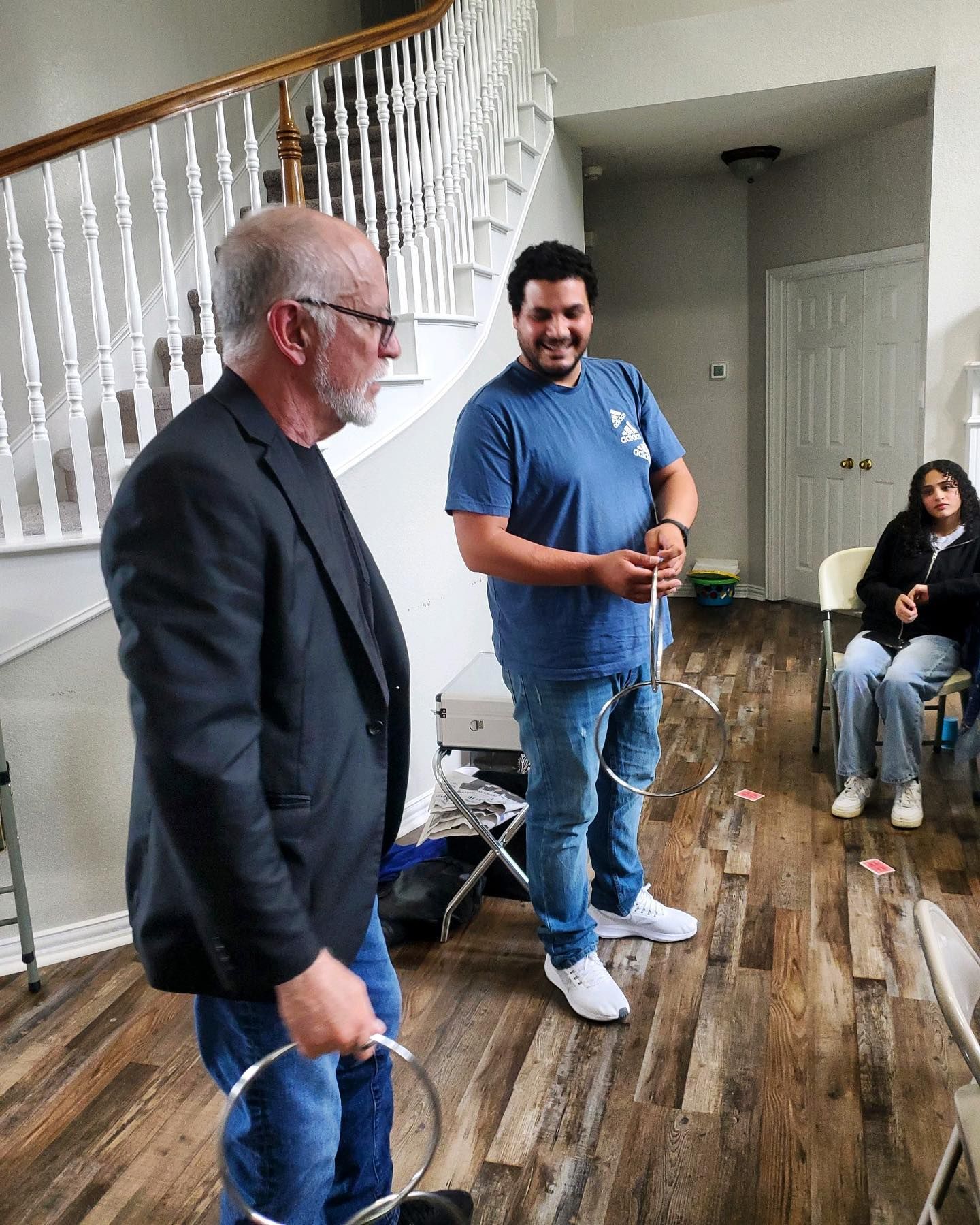 Two men are standing in a living room with a woman sitting in a chair.