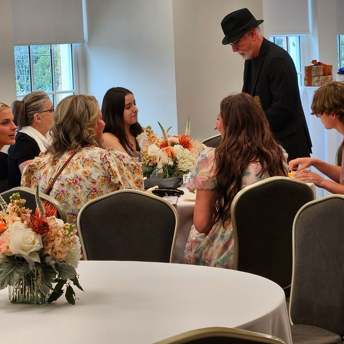 A group of people are sitting around a table with flowers on it.