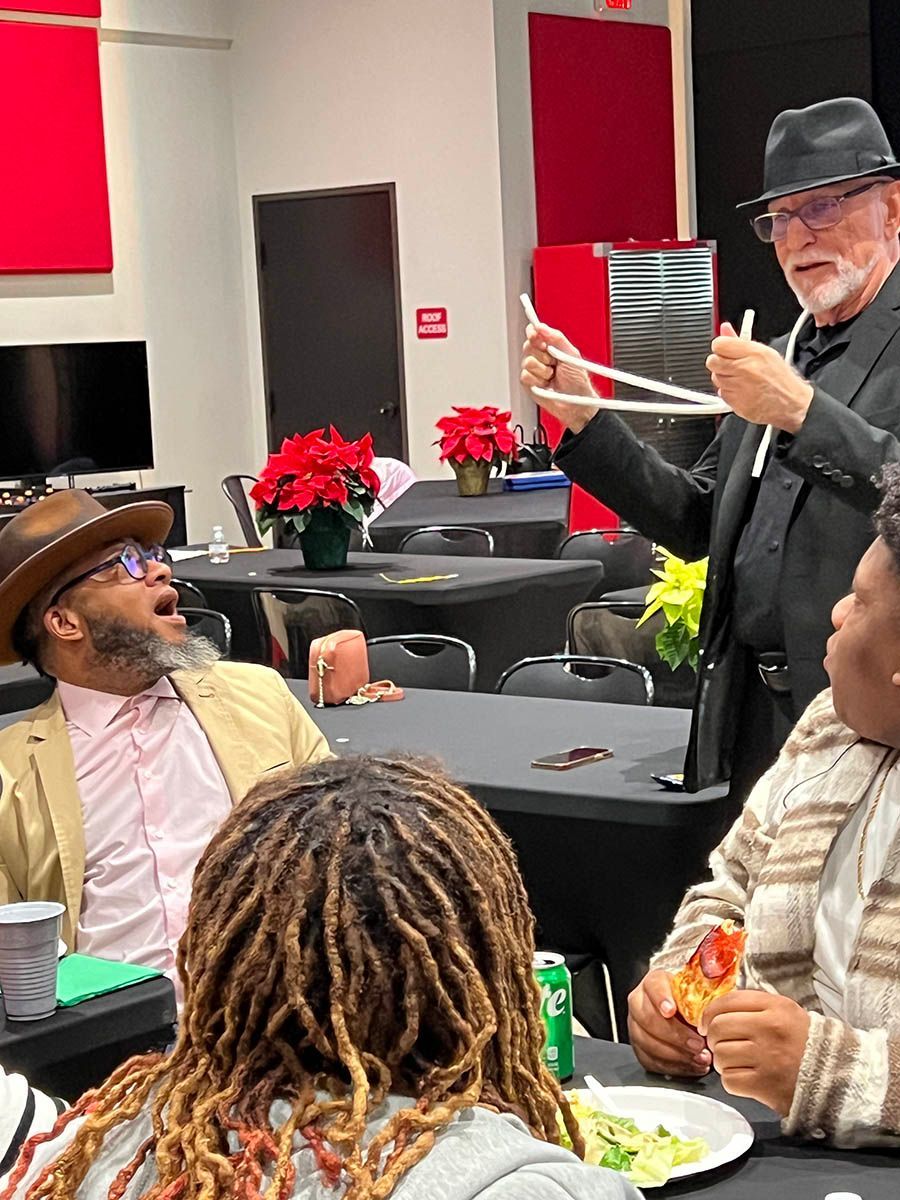 A group of people are sitting at tables in a room while a man performs a magic trick.