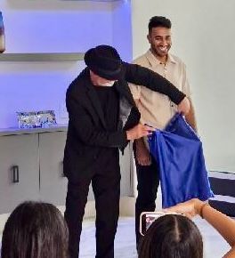 A man is holding a blue shirt in front of a group of people.