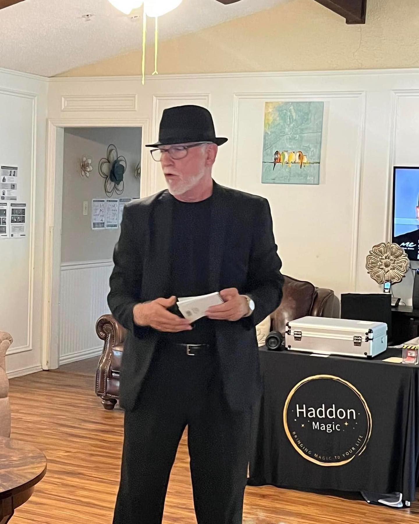 A man in a suit and hat is standing in a living room holding a piece of paper.