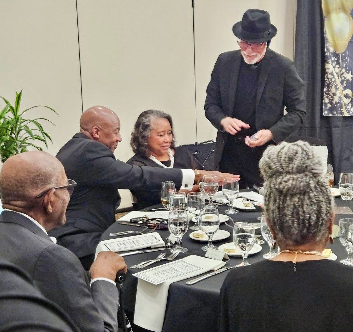 A man in a black hat is talking to a group of people at a table.