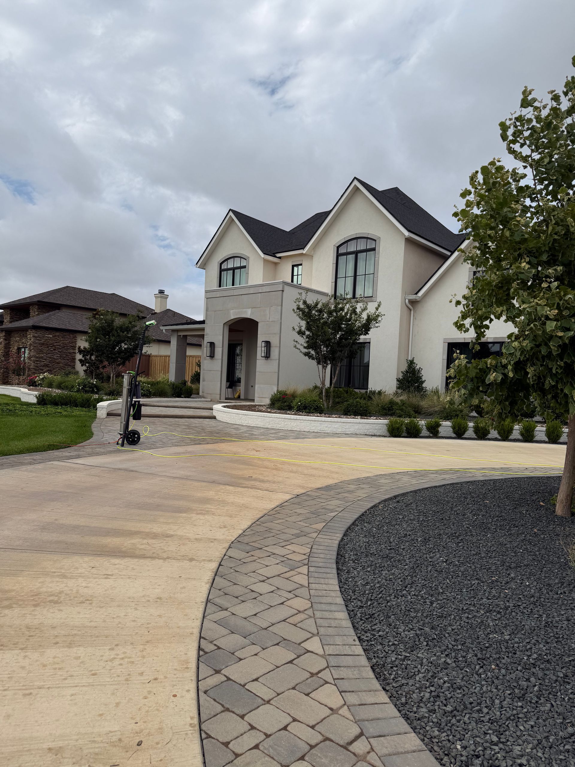 Modern two-story house with arched entry, stone driveway, and cloudy sky