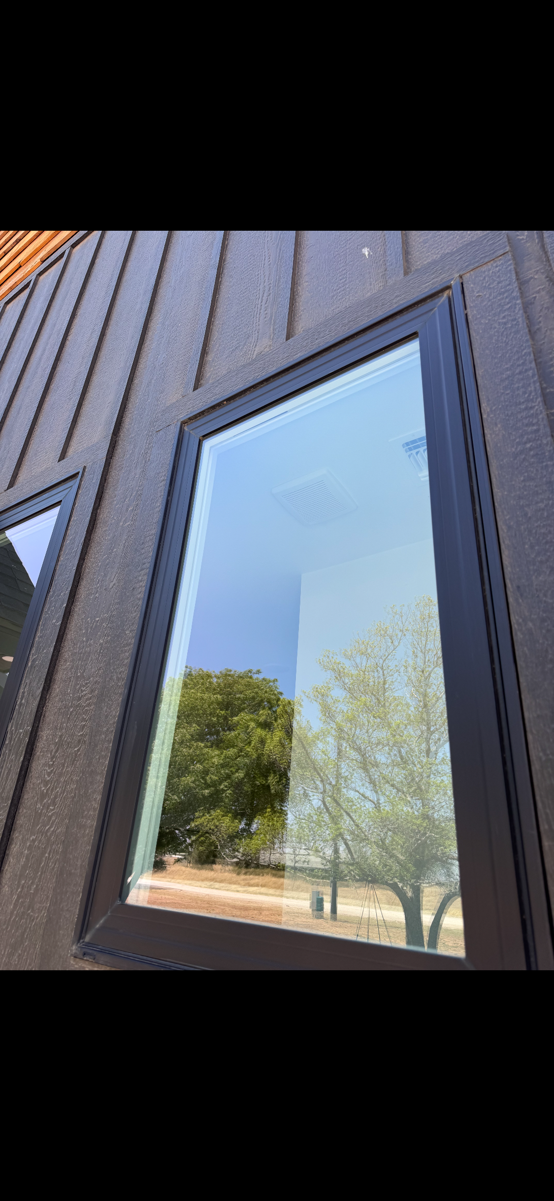 Exterior wall with reflective window showing trees and blue sky