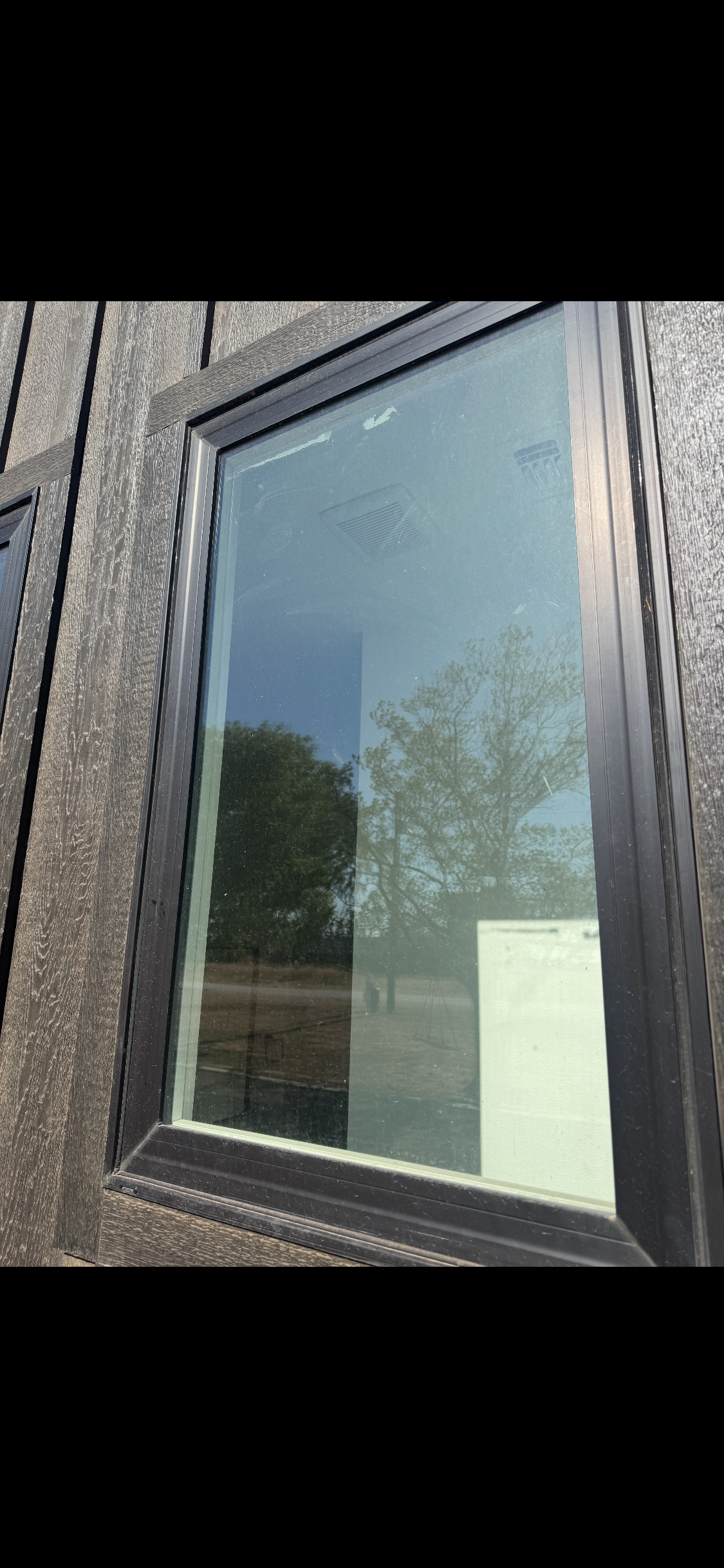 Reflective glass window in a dark brick building facade with a small posted notice