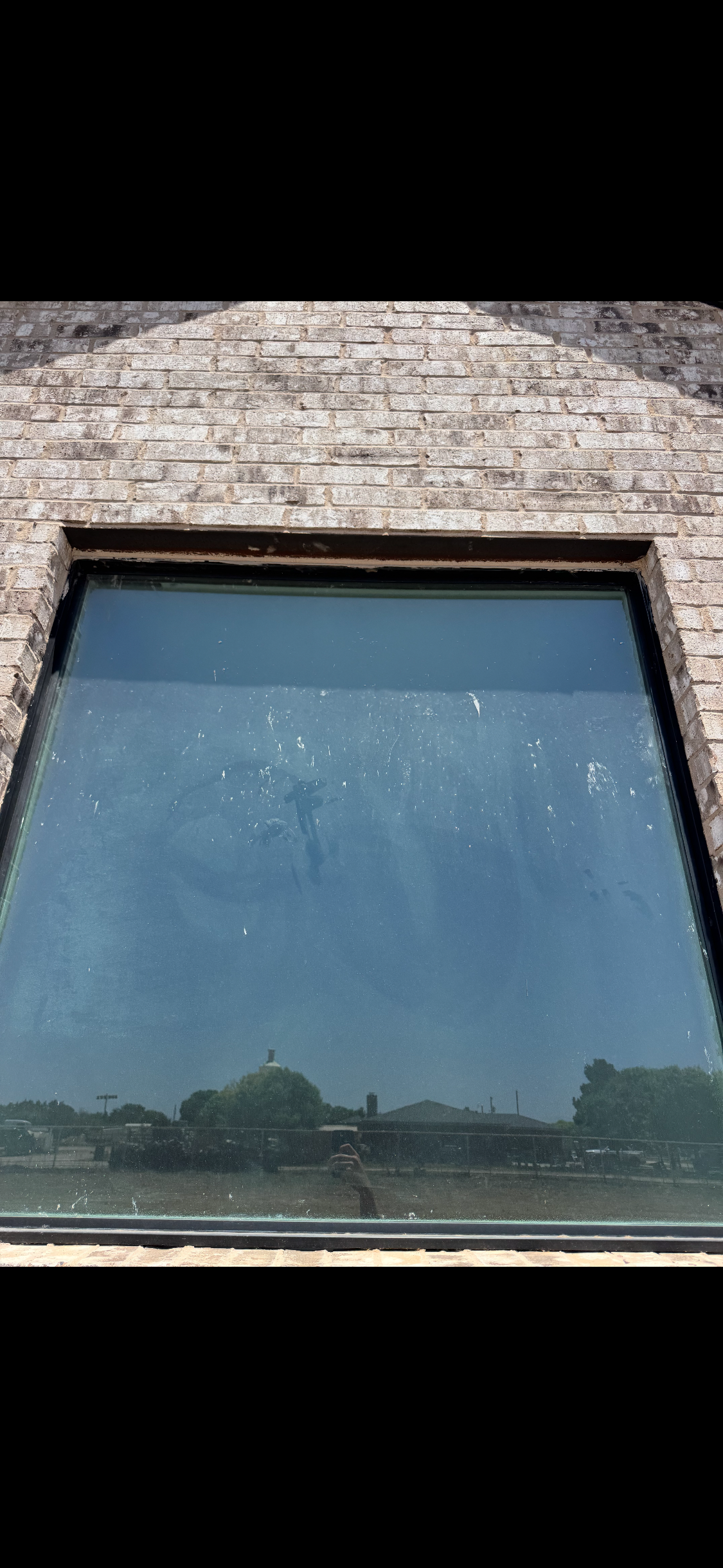 Large window set in a stone wall reflecting blue sky and trees