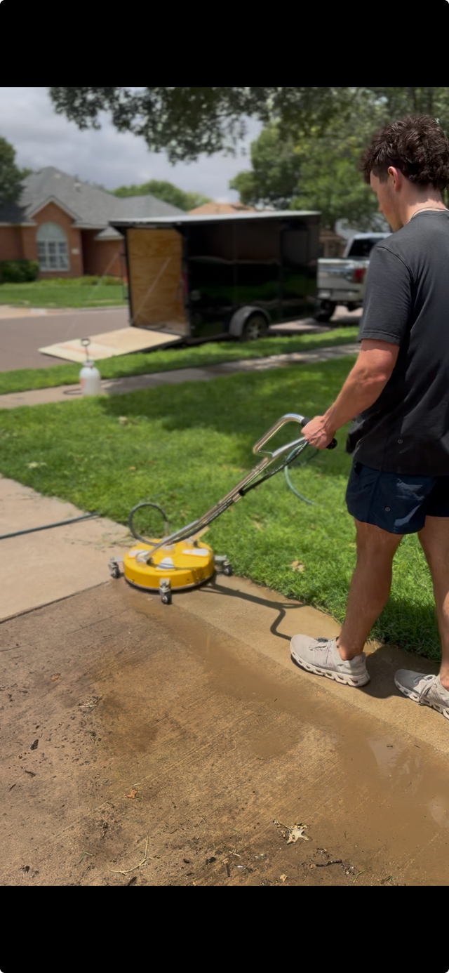 Person using a yellow pressure washer on a driveway in front of a suburban house