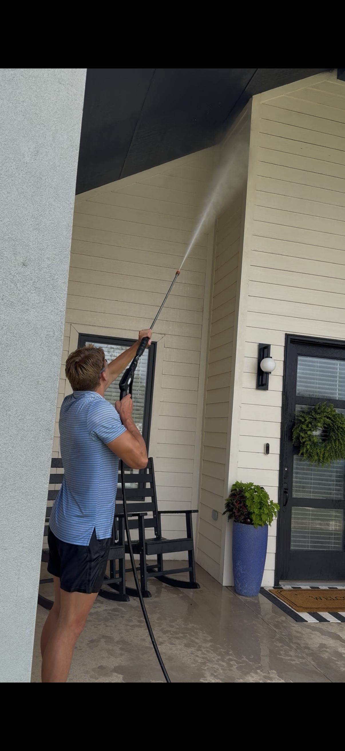 Man using a long pole to clean or paint a tall exterior wall under a covered entrance