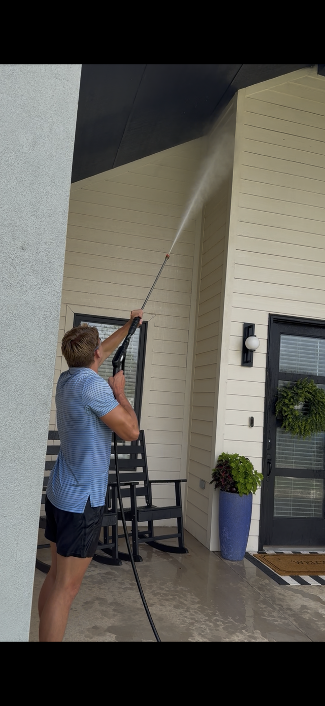 Man using a long pole to clean or paint a tall exterior wall under a covered entrance