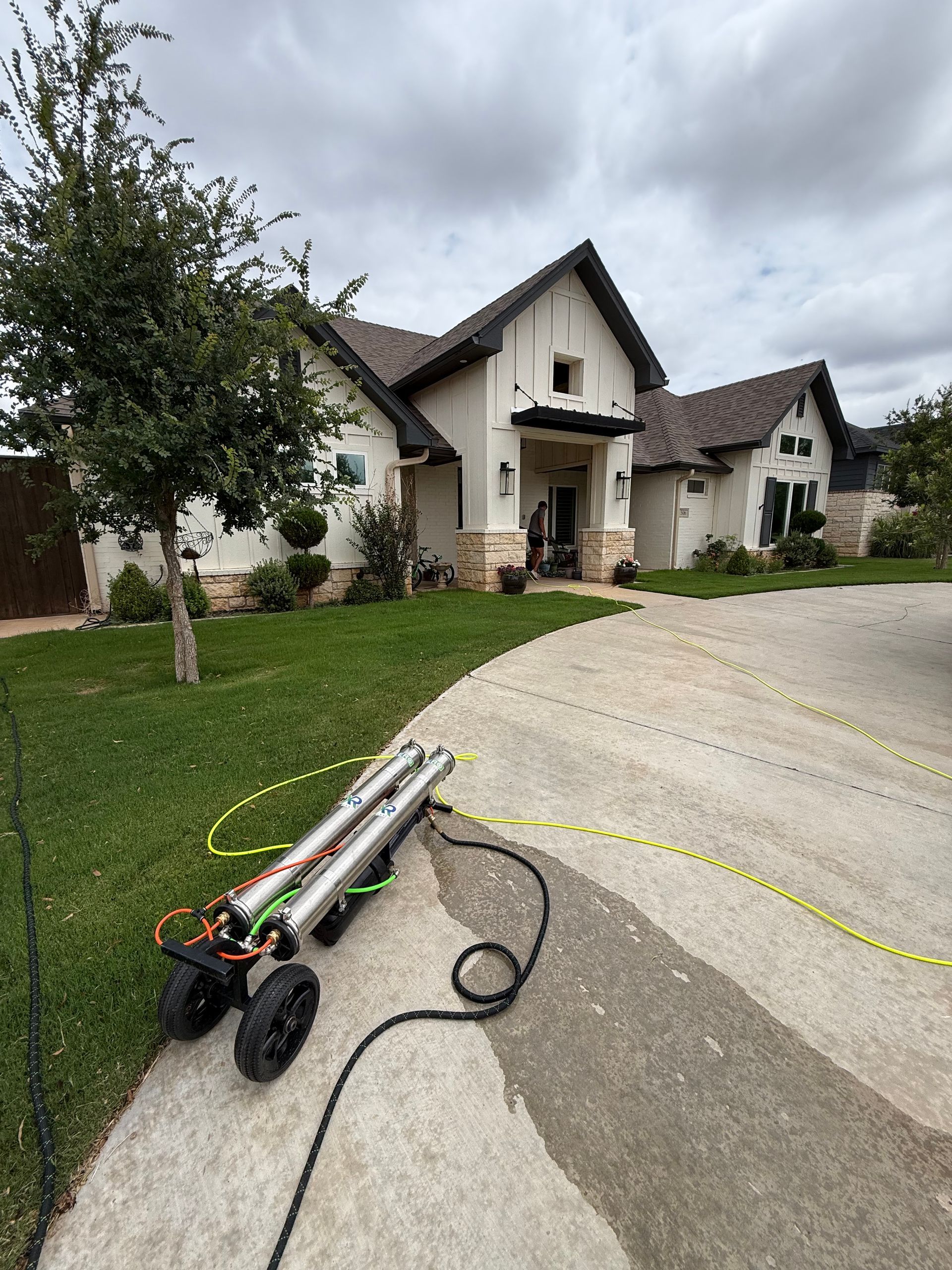 Leaf blower on driveway in front of a suburban house and lawn.