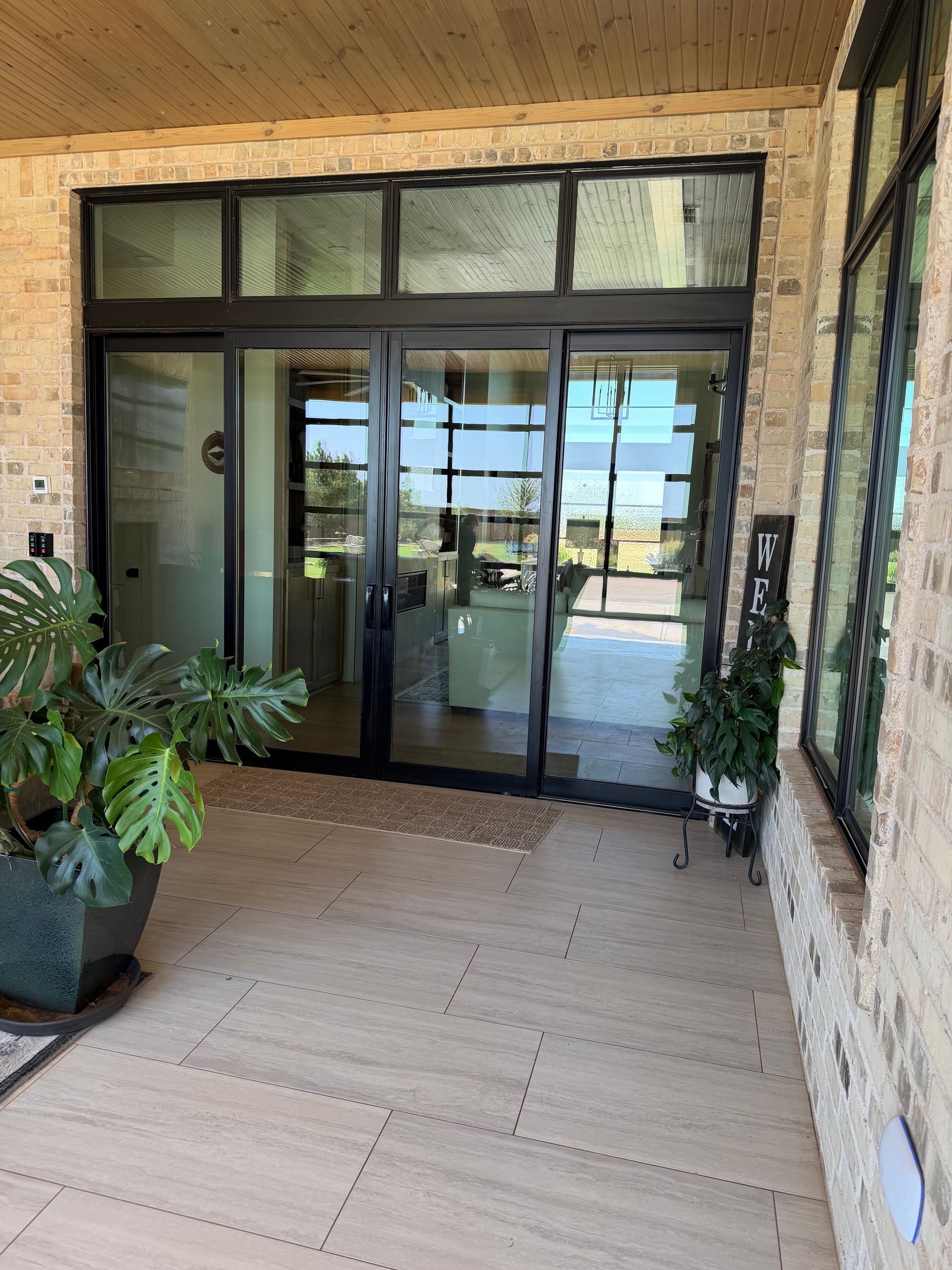 Covered entrance with glass sliding doors, potted plants, and tan tile flooring