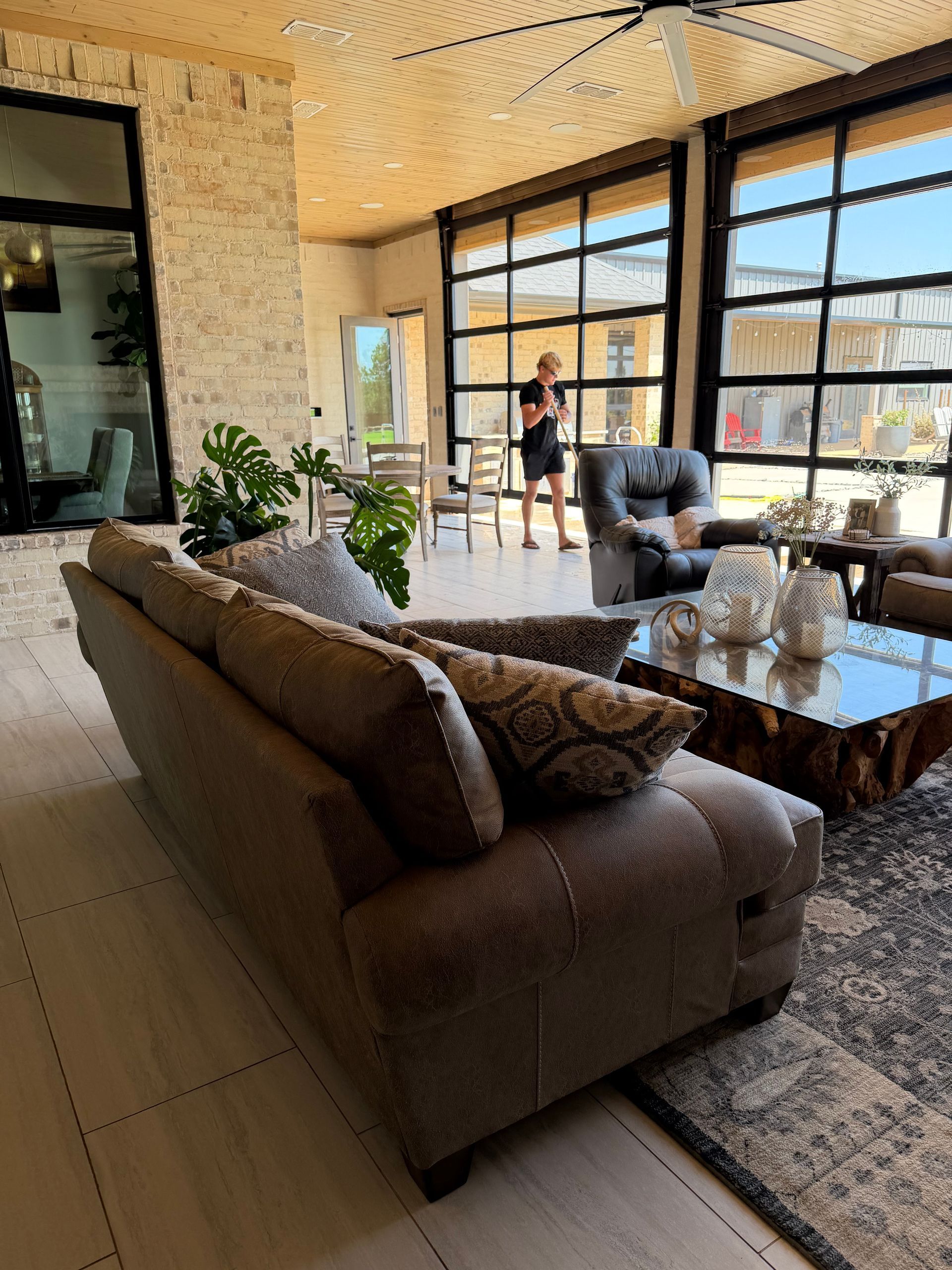 Modern living room with a brown sofa, glass coffee table, and large windows overlooking a sunny view